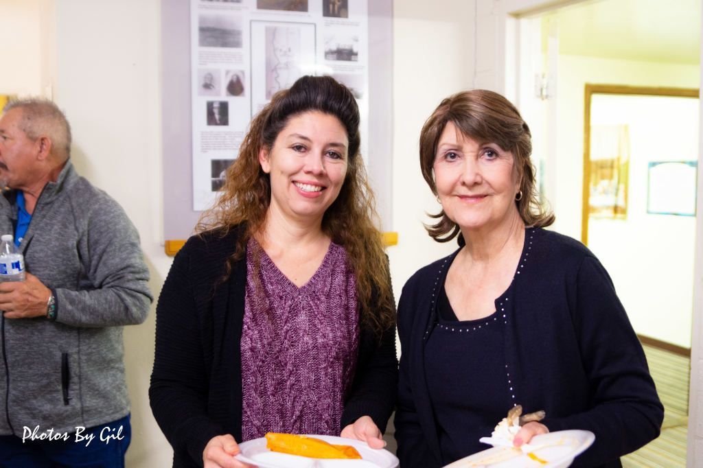 Two women at a gathering, smiling warmly while holding plates of food. 