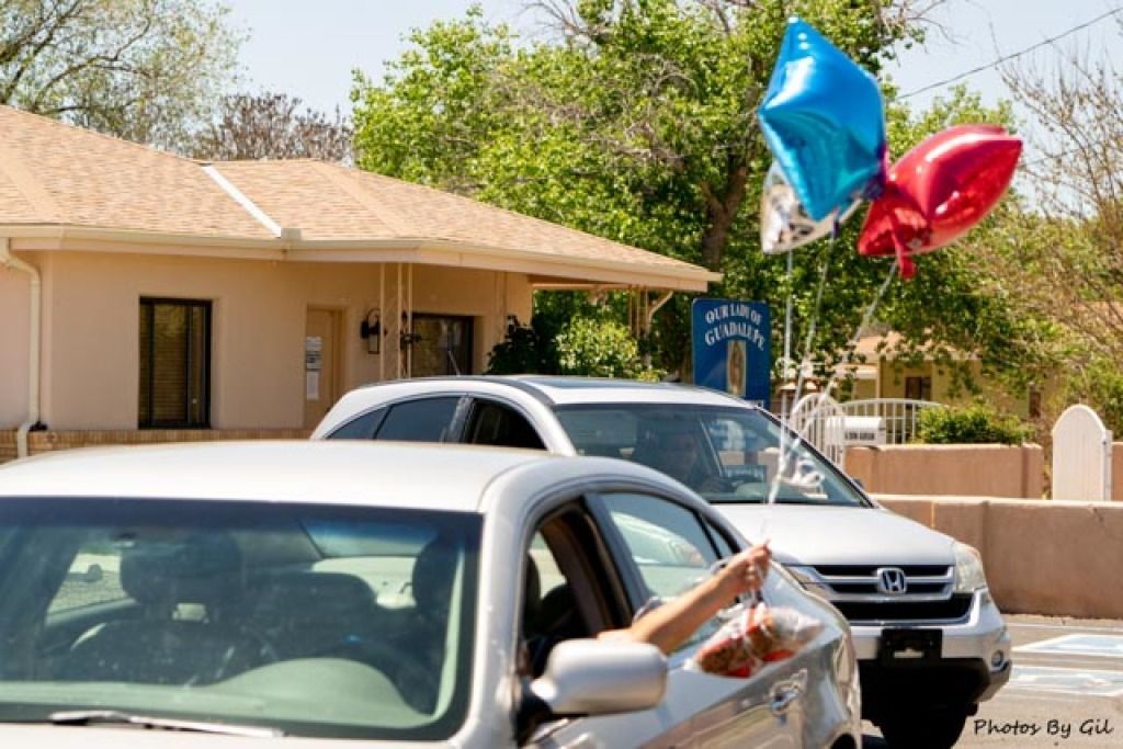 A car in a parking lot with a person’s hand holding colorful balloons out the window.