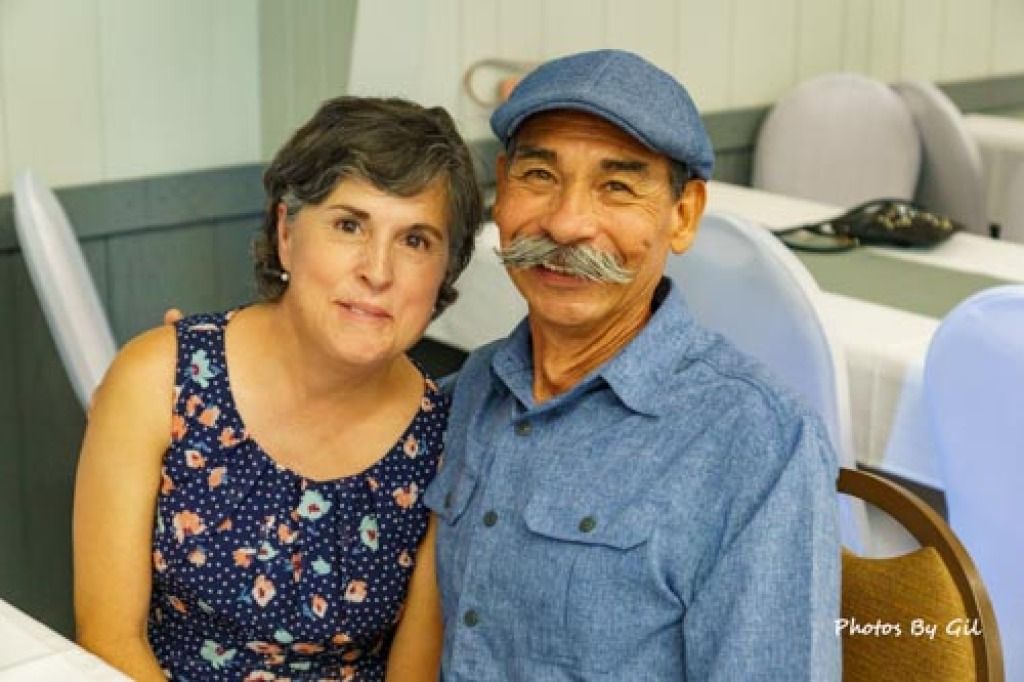 A smiling couple sits closely together indoors. 
