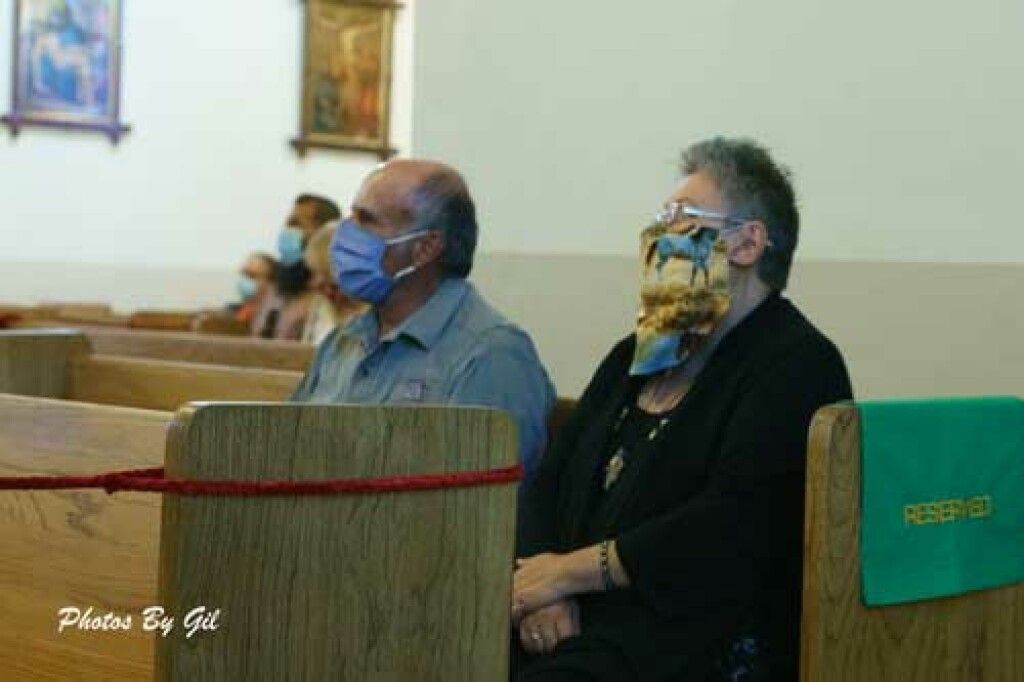 Two people sit in a church pew wearing face masks. 