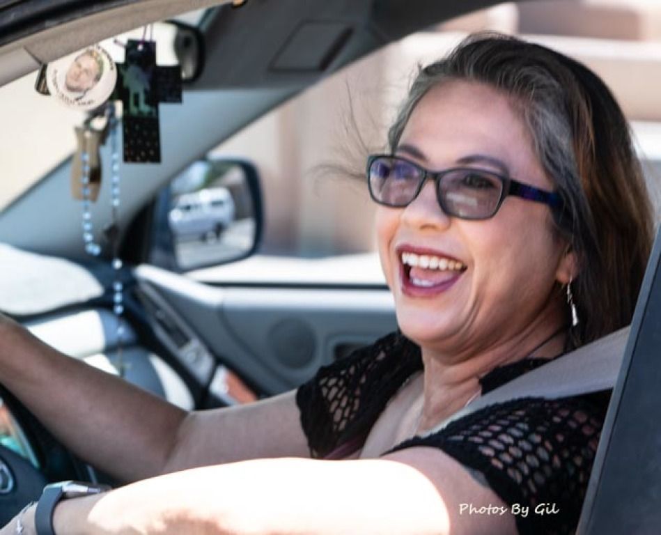 A woman with long hair and glasses is joyfully laughing while driving a car. 