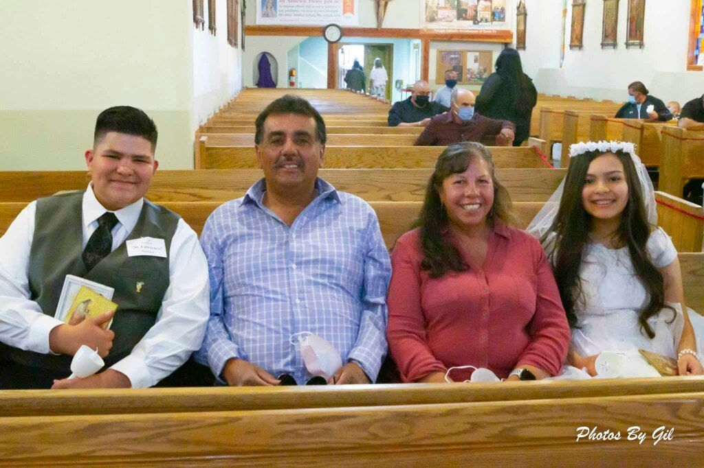 A boy in a suit holds a prayer book, while a girl in a white dress and veil sits beside an older couple. 