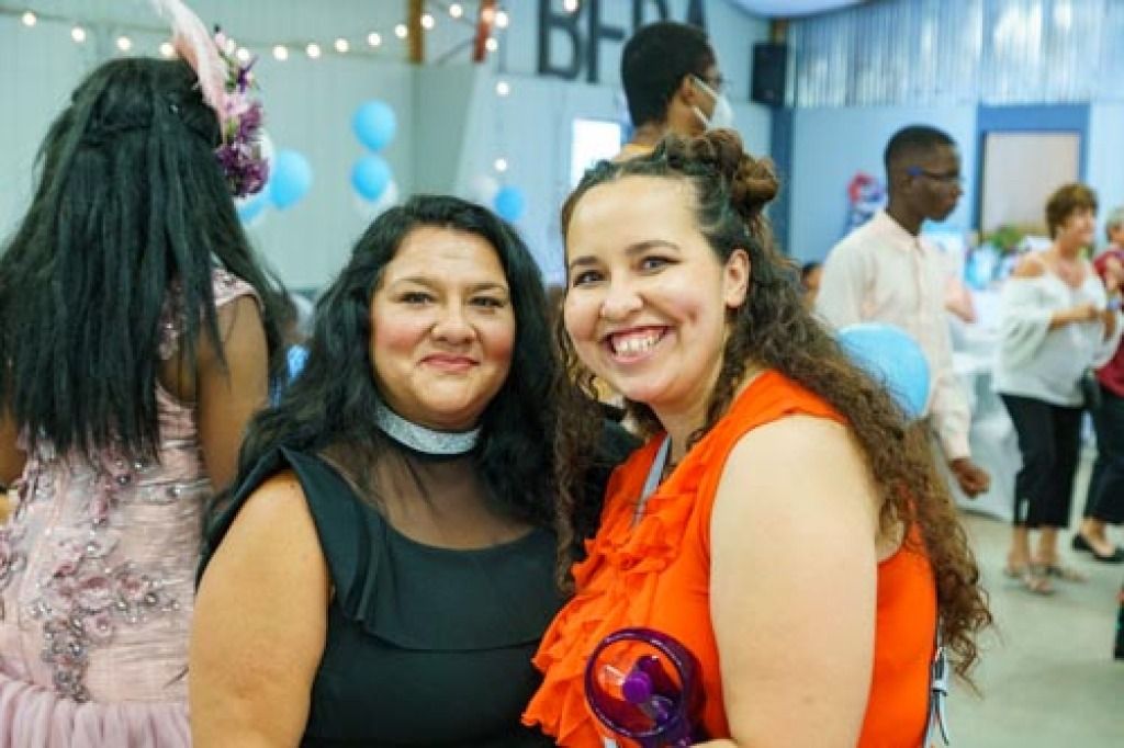 Two women smiling at a festive indoor event.