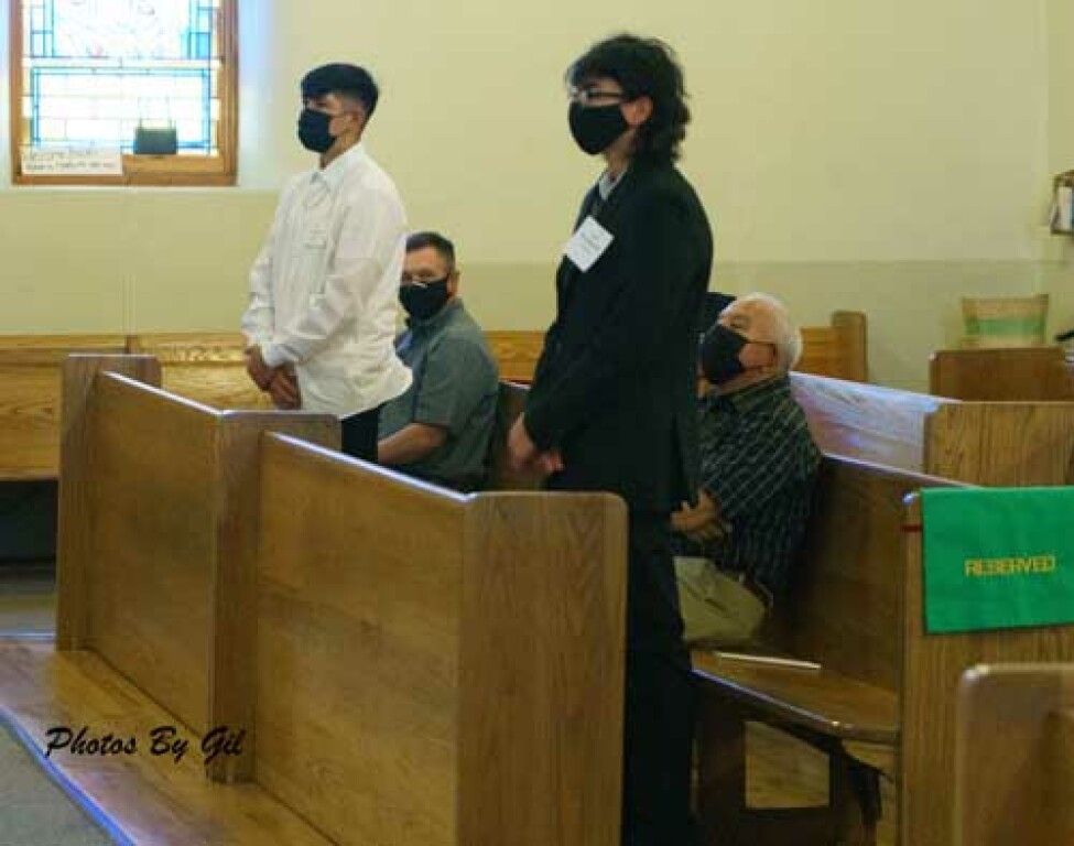 Two people in a church, wearing black masks; one in a suit, the other in white. 