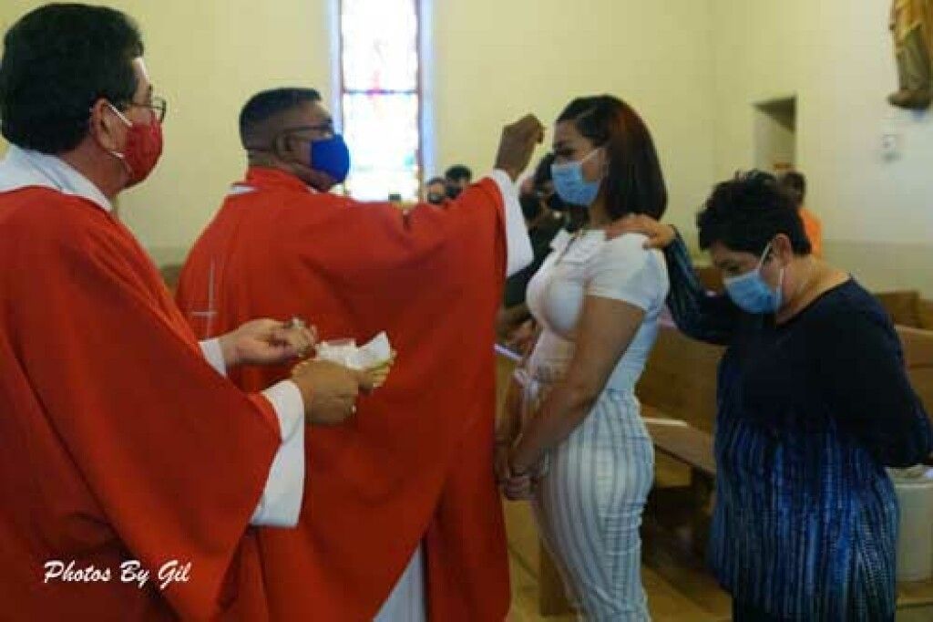 A priest in a red robe performs a ritual on a woman in a church. 