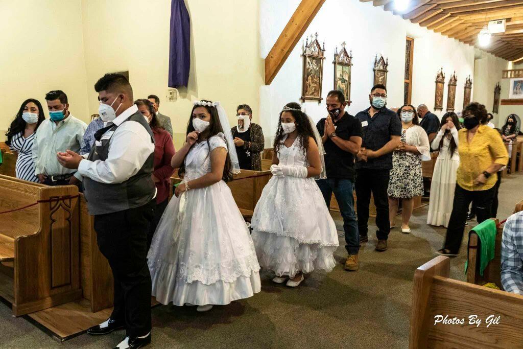 A church interior shows a group of people standing in line, wearing masks.