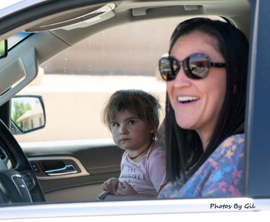 A woman wearing sunglasses smiles joyfully in the driver's seat of a car.