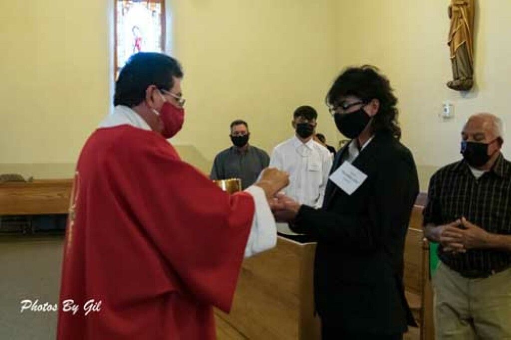 A priest in a red vestment gives communion to a person in black at a church service. 