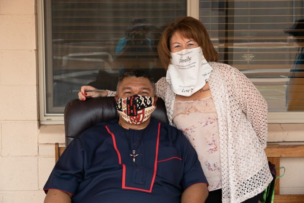 A couple stands in front of a brick wall, both wearing decorative face masks.