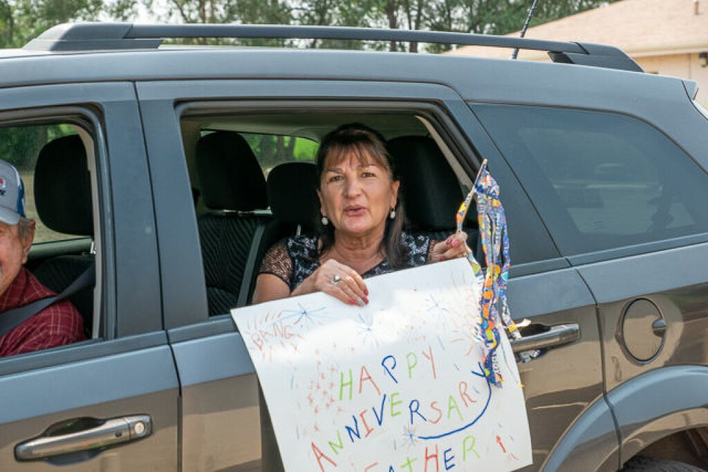 Woman inside a car holds a colorful banner and streamers.