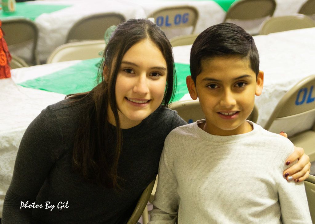 A young woman and a boy smile warmly at a gathering.