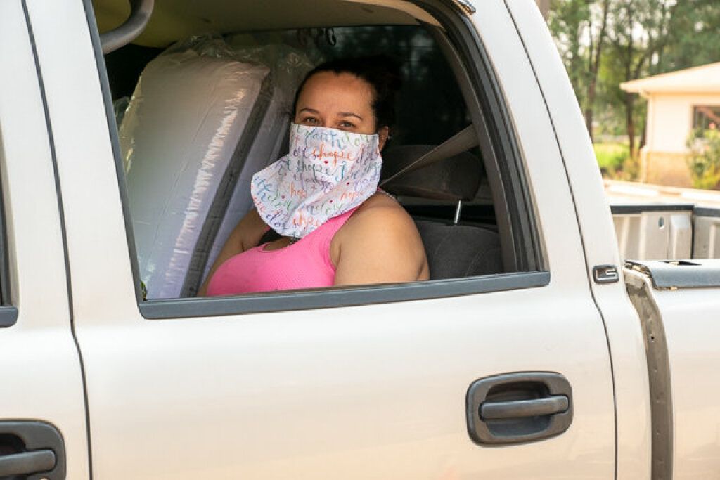 A woman in a pink tank top sits in a white truck, wearing a colorful face mask.