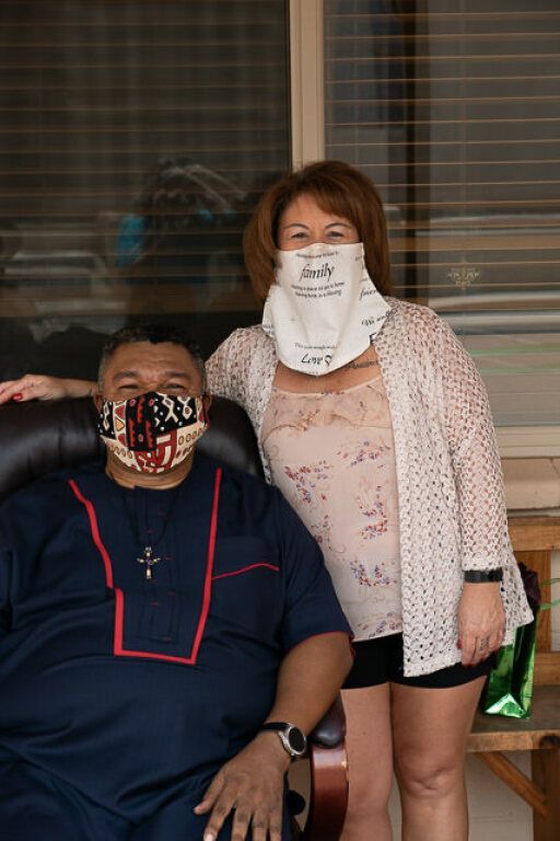 A man and woman wearing patterned face masks pose together outdoors. 