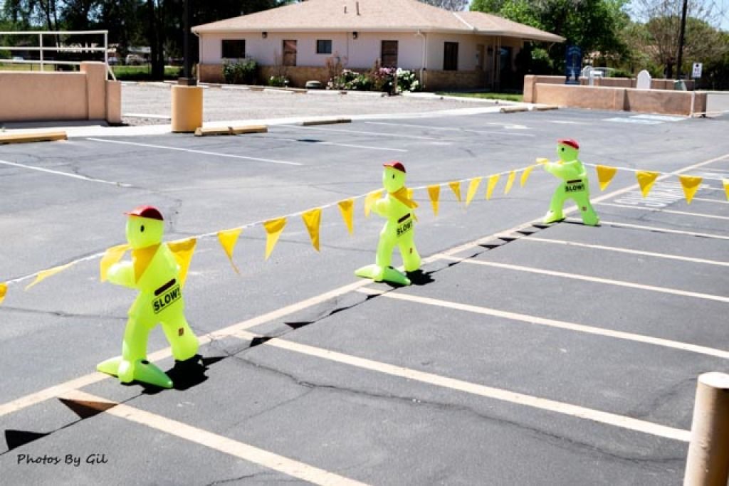 Three neon green safety figures in a parking lot hold yellow flags, creating a barrier. 