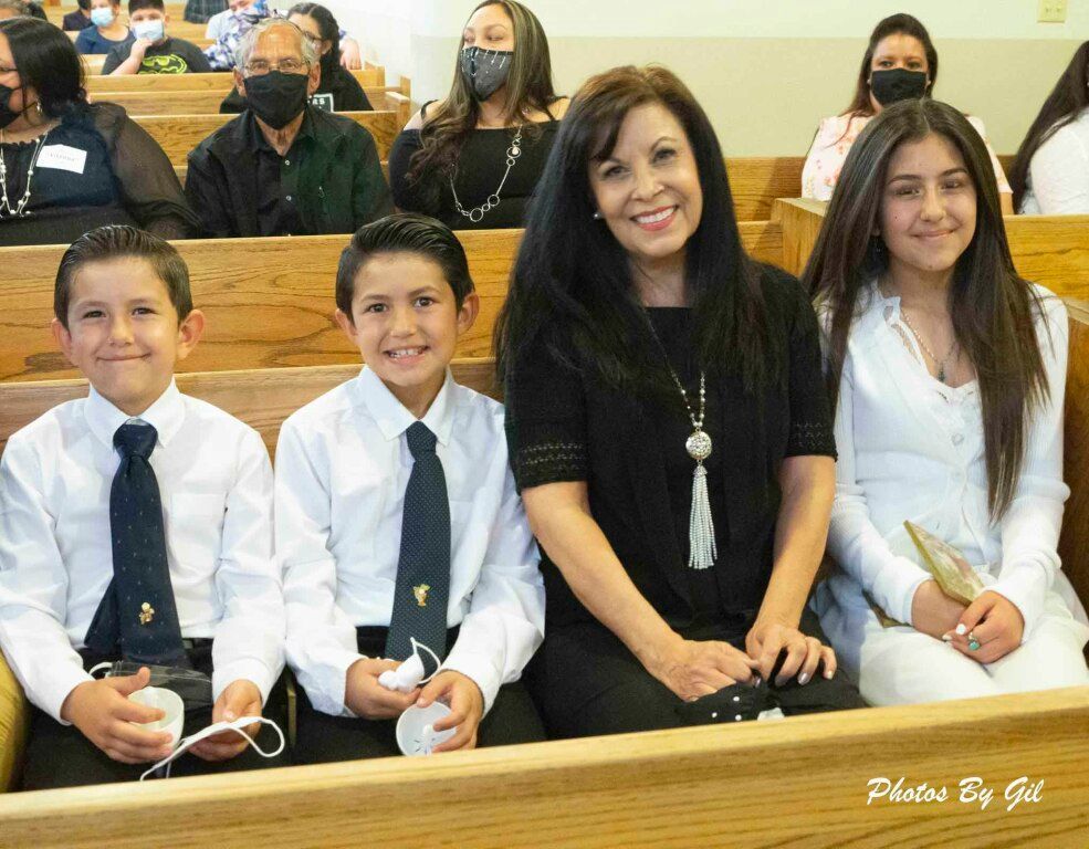 A smiling woman sits between three children in church pews.
