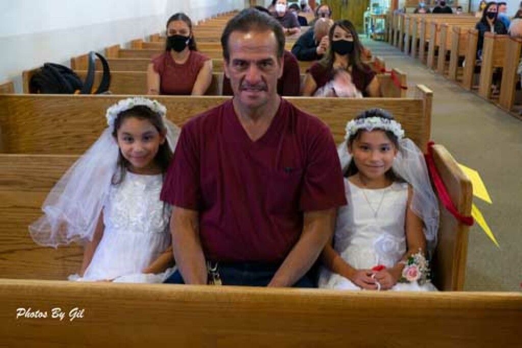 A man sits between two young girls in white dresses and veils.