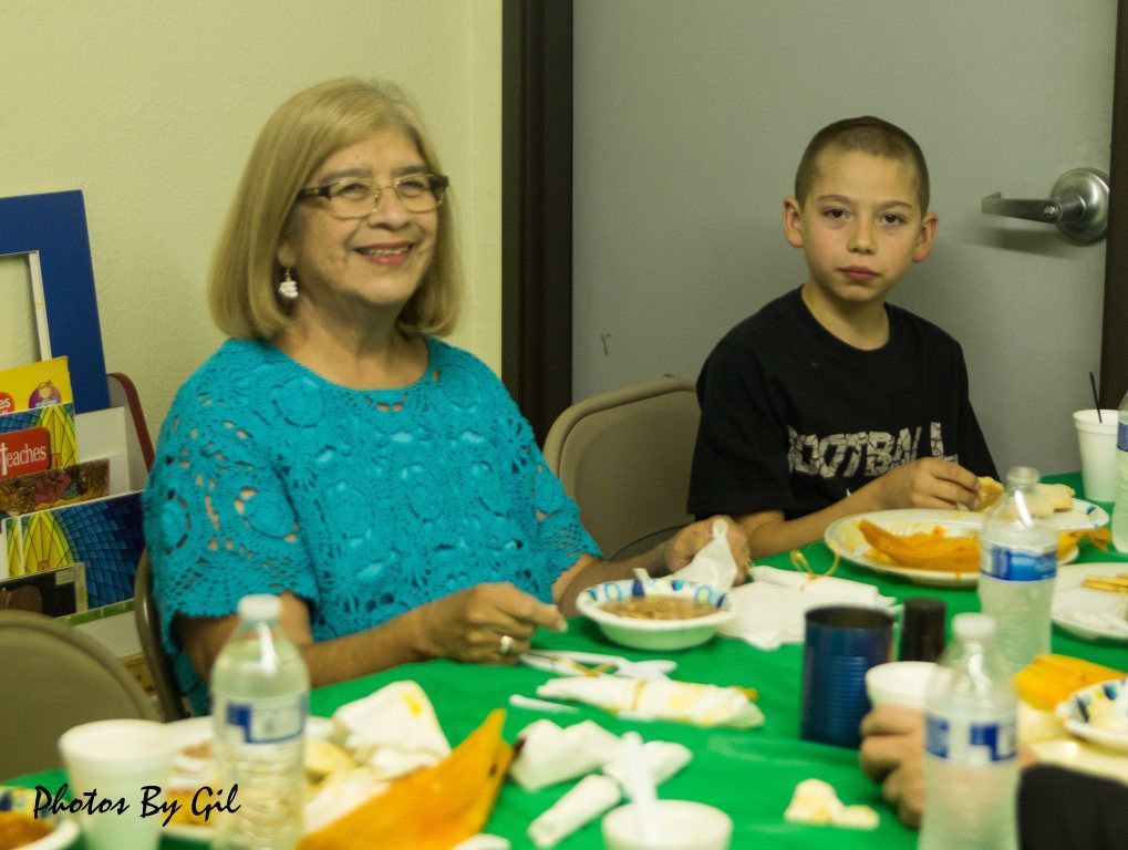 A smiling woman in a blue top and a young boy sit at a table with food.