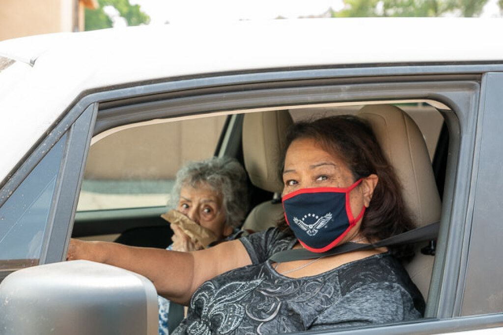 A woman in a car wears a patterned face mask, smiling with eyes. 