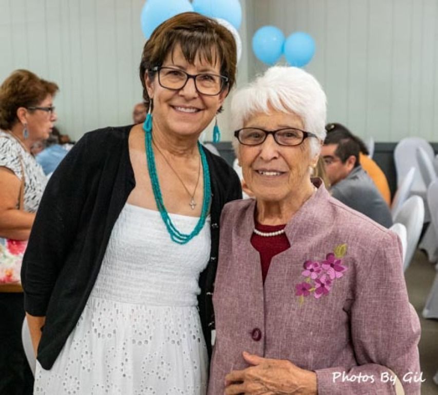 Two smiling women stand together at an event, wearing glasses.