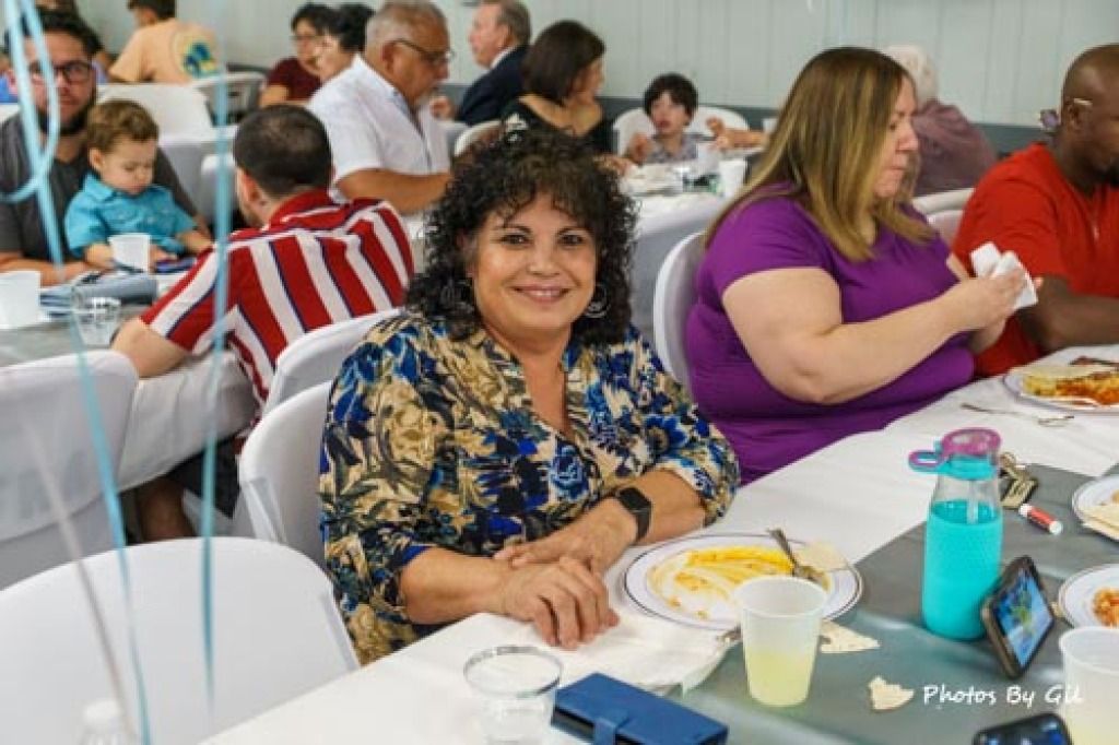 A woman in a floral blouse smiles at a table with others enjoying a meal.