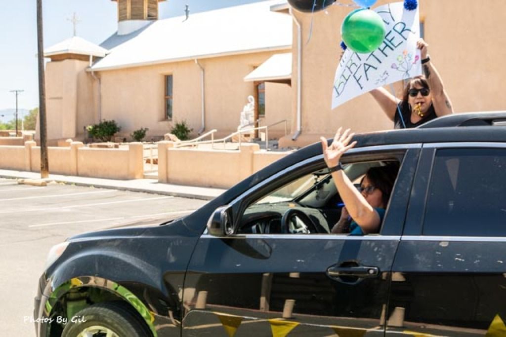 A black car with passengers celebrating outside a beige church.