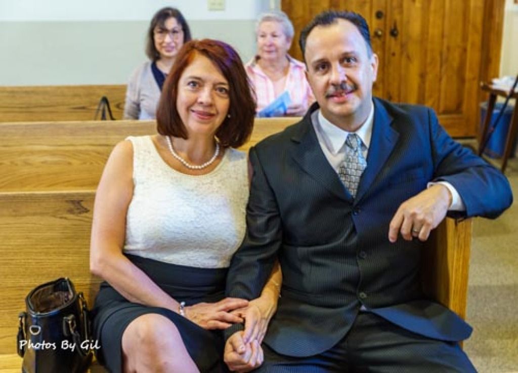 A couple sits on a wooden bench, smiling warmly. 