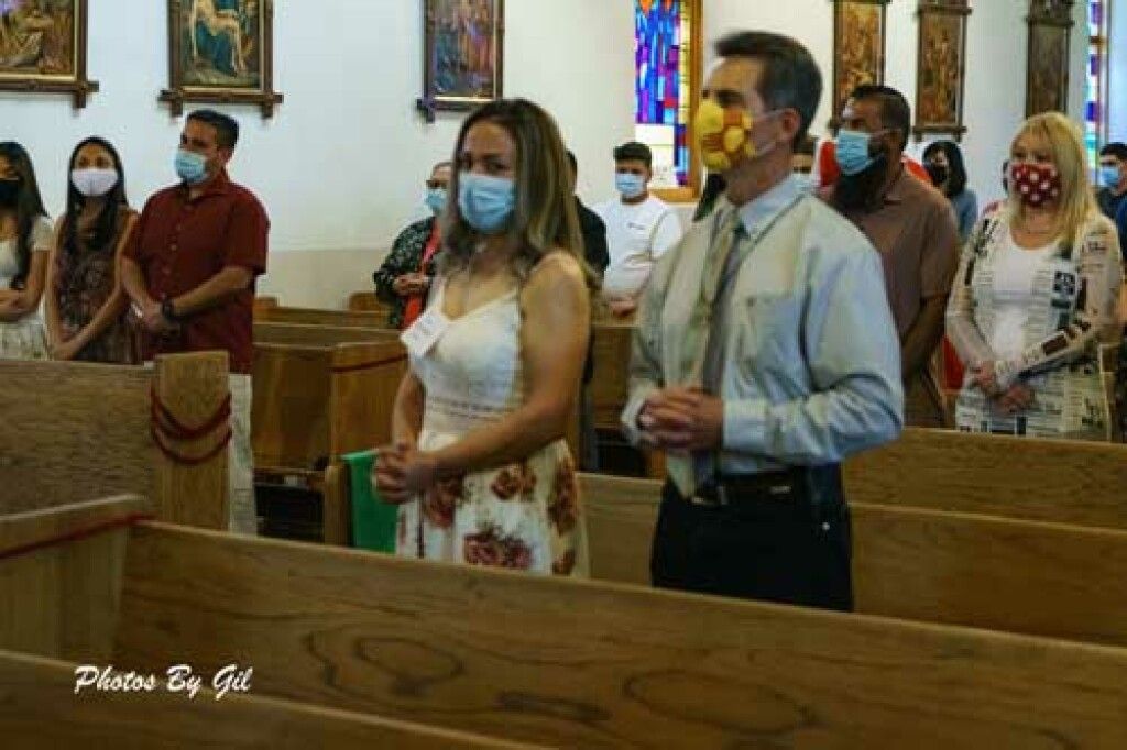People wearing masks stand in wooden pews inside a church.