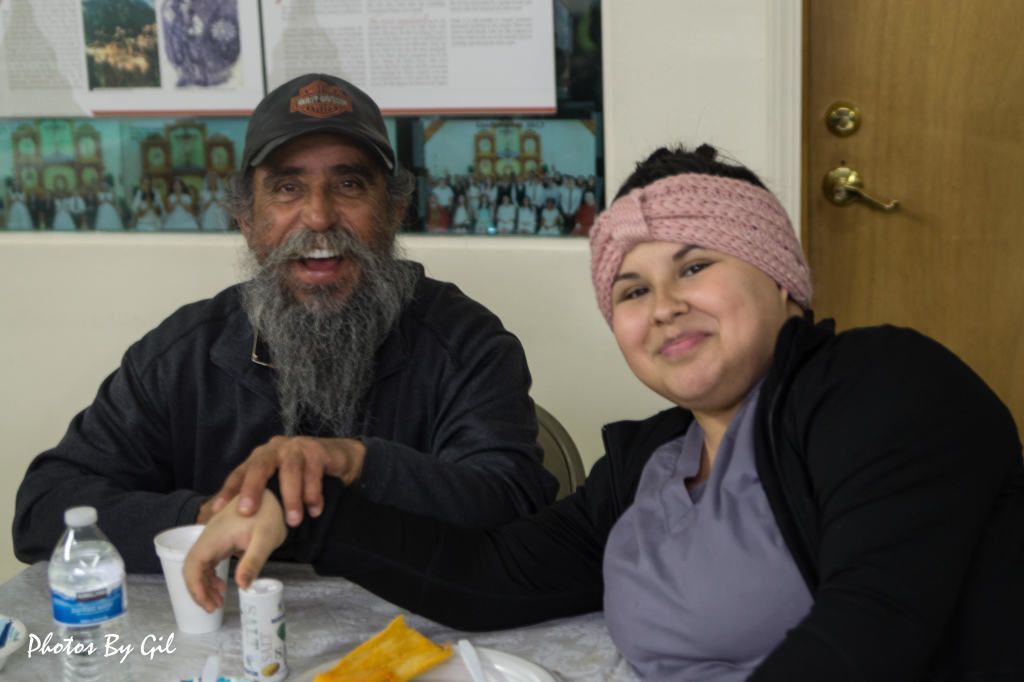 A man and a woman sit at a table smiling warmly.
