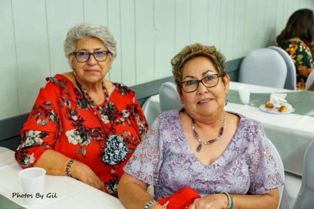 Two older women seated at a table, smiling warmly. 