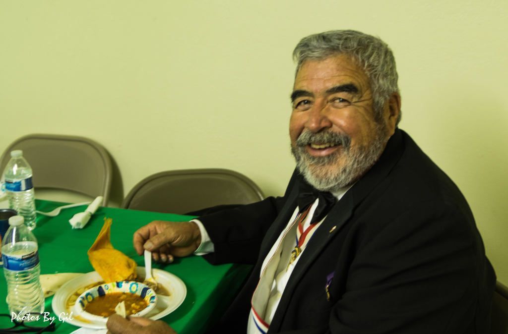 A smiling man with gray hair and a beard sits at a table.
