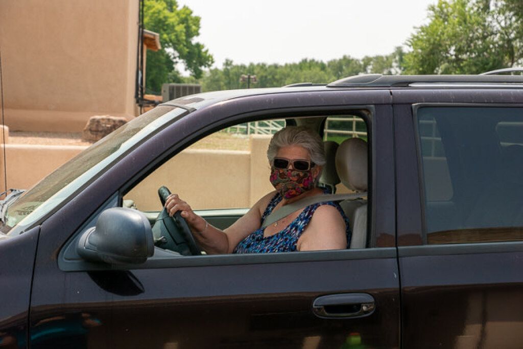 A woman in a patterned face mask and sunglasses sits in a parked SUV.