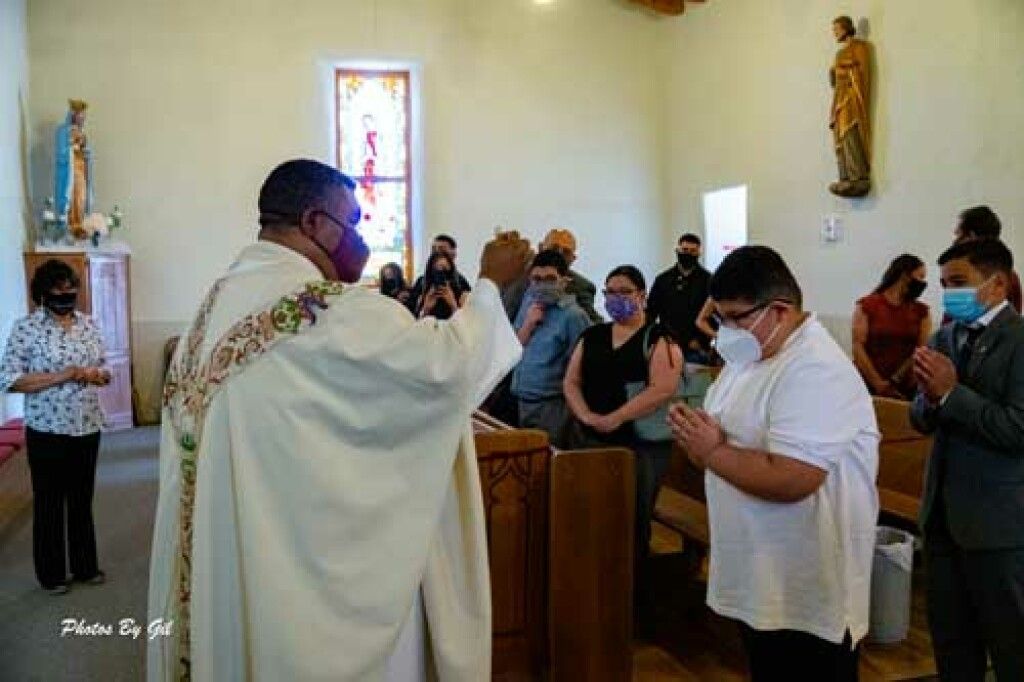 A priest in a white robe conducts a service in a church.