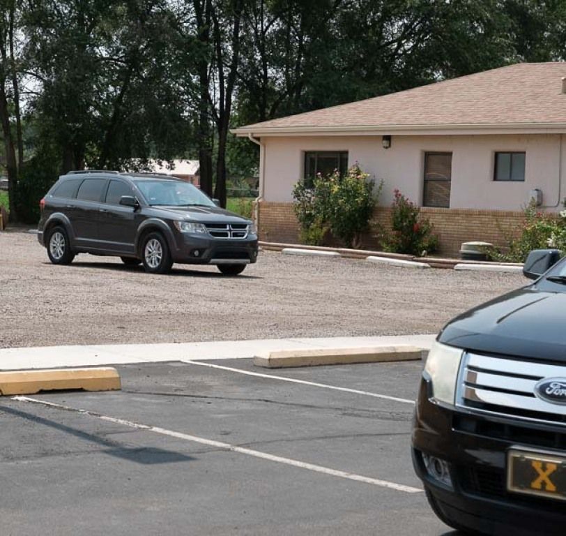 A dark SUV is parked in a gravel lot beside a building with beige siding.