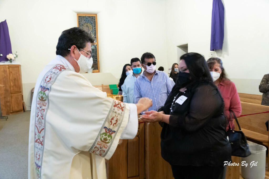 A priest in ornate robes gives communion to a masked woman in a church.