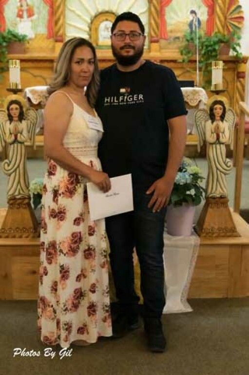 A couple stands in front of a decorated altar with angel statues and plants.