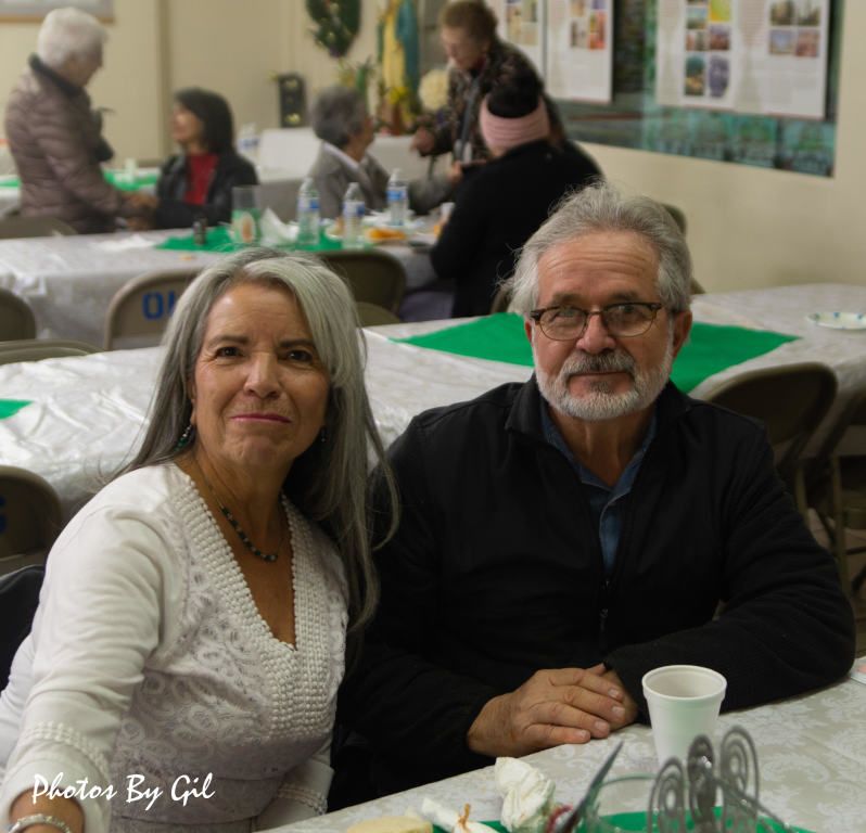 An older couple sits together at a table during a social gathering.