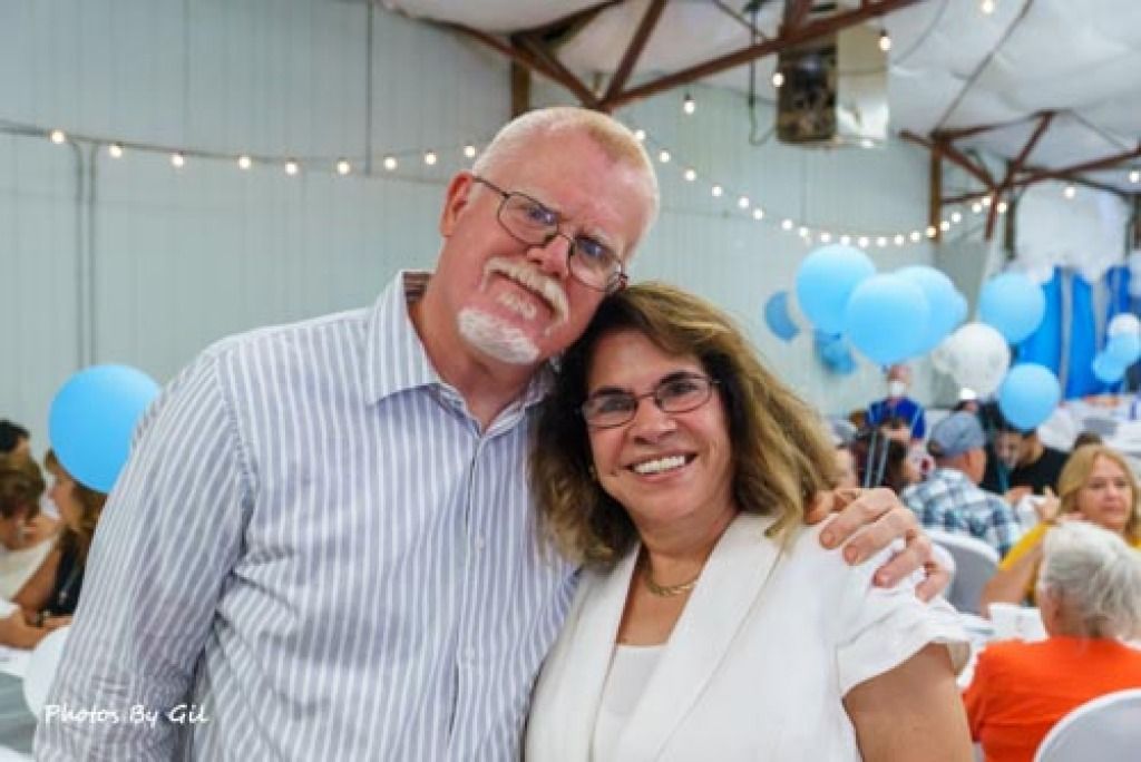 A smiling man and woman pose together at a festive indoor event.