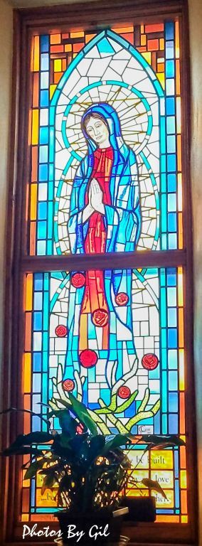 A stained glass window depicts a serene figure in blue and red, hands in prayer. 