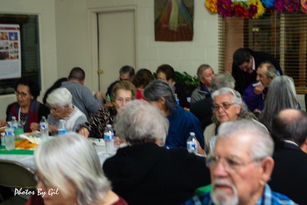 A gathering of elderly people seated around tables, enjoying a meal. 