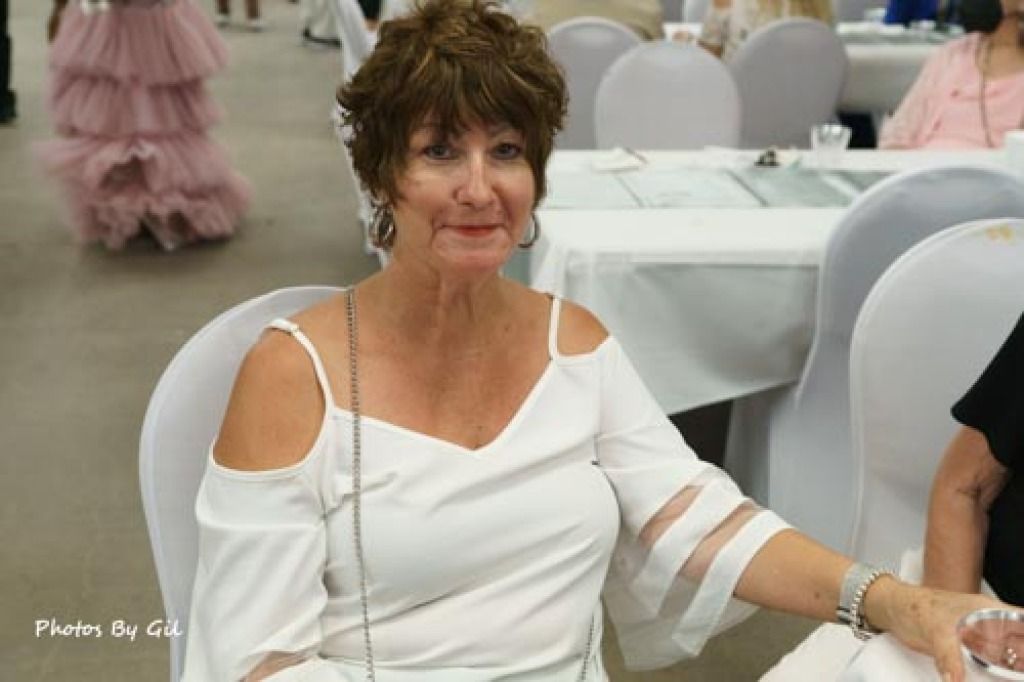 Woman in white cold-shoulder top seated at a table, smiling. 