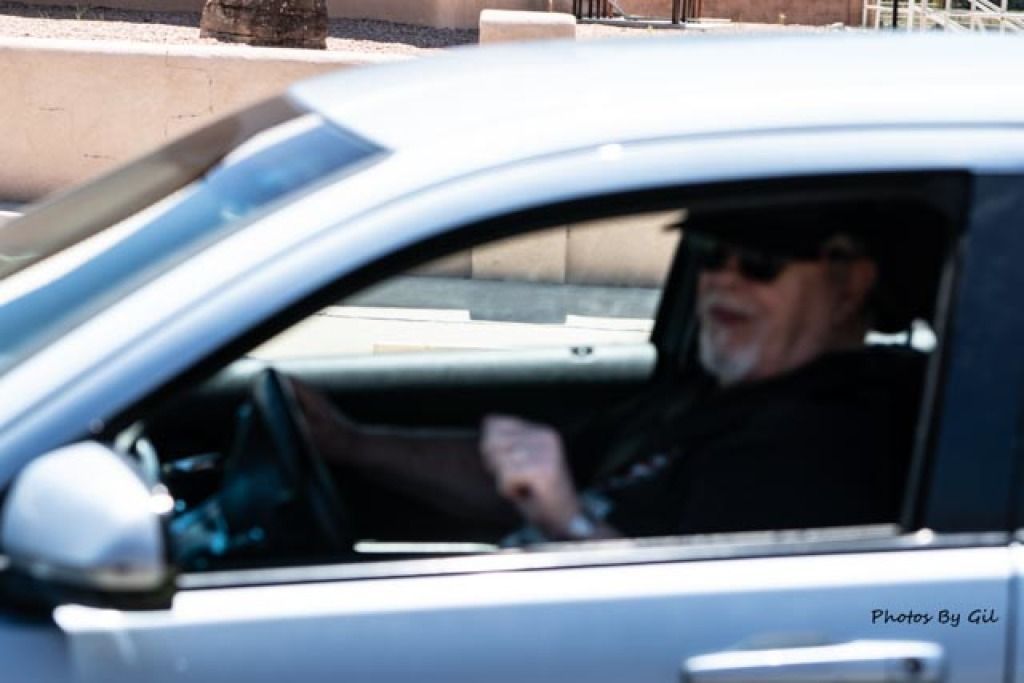 Blurry photo of a person in sunglasses driving a silver car.
