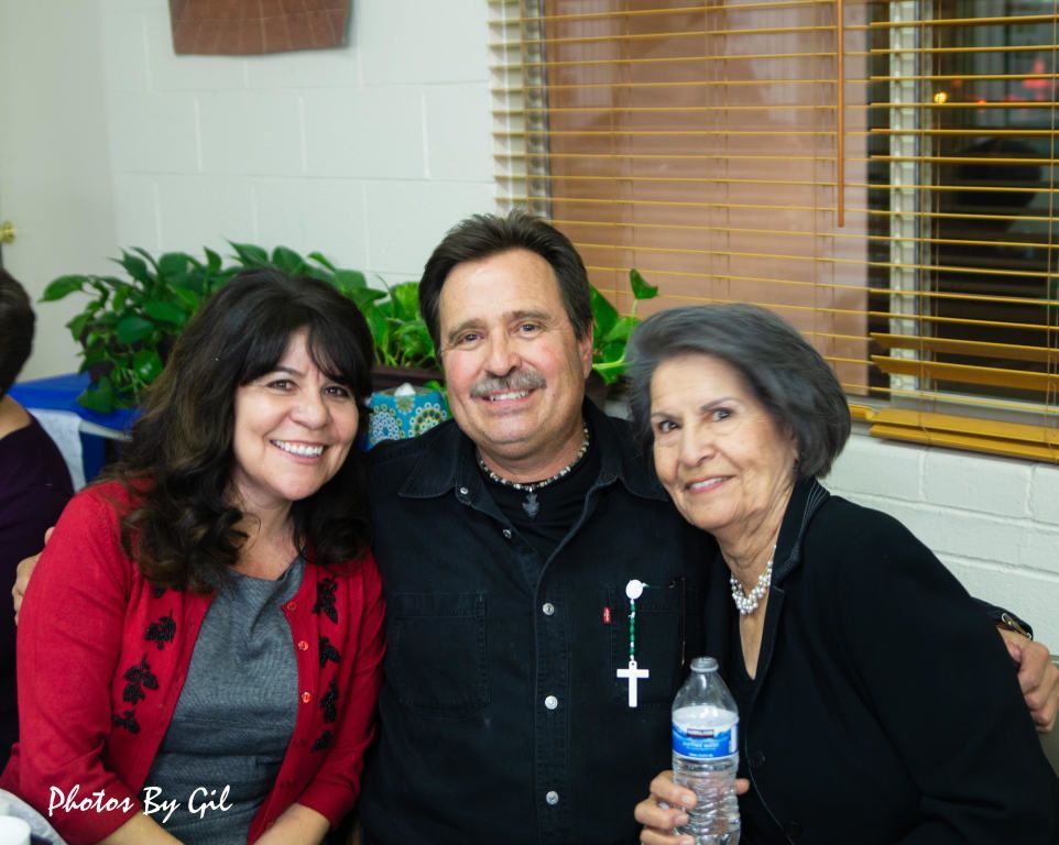 A group of three people smiling warmly, sitting closely indoors.