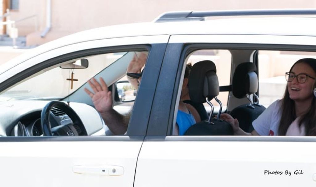 A woman wearing glasses smiles in the back seat of a white car. 