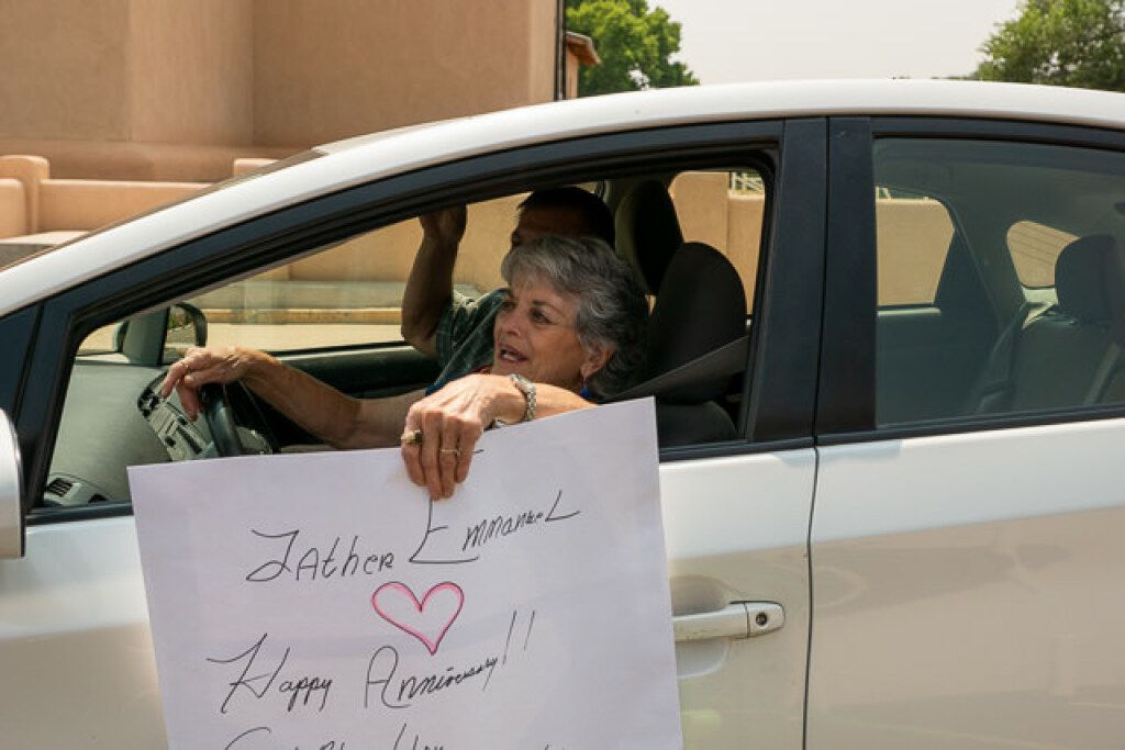 An elderly woman smiling in a car holds a handwritten sign.