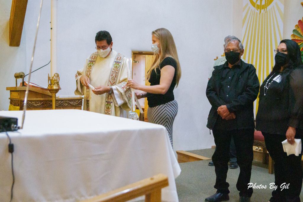 A priest in a white robe leads a masked ceremony with three attendees in a church. 