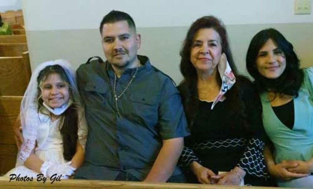 A smiling girl in a white dress and veil on the left, with three adults beside her.