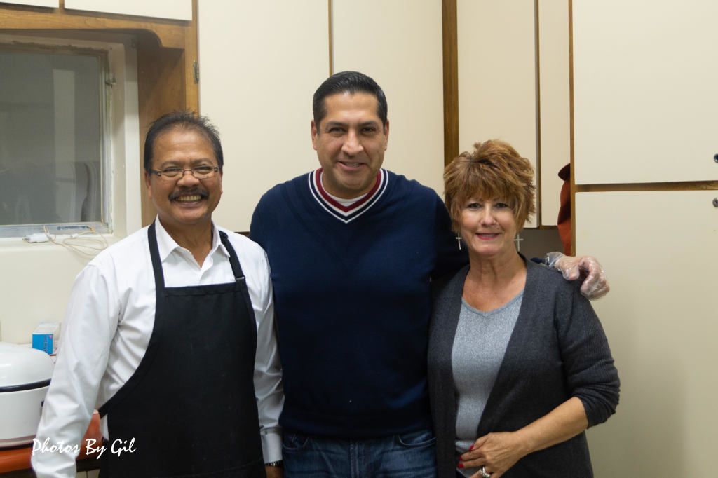 Three people stand together, smiling.