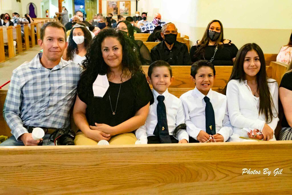 A family of five smiles while sitting in a church pew. 