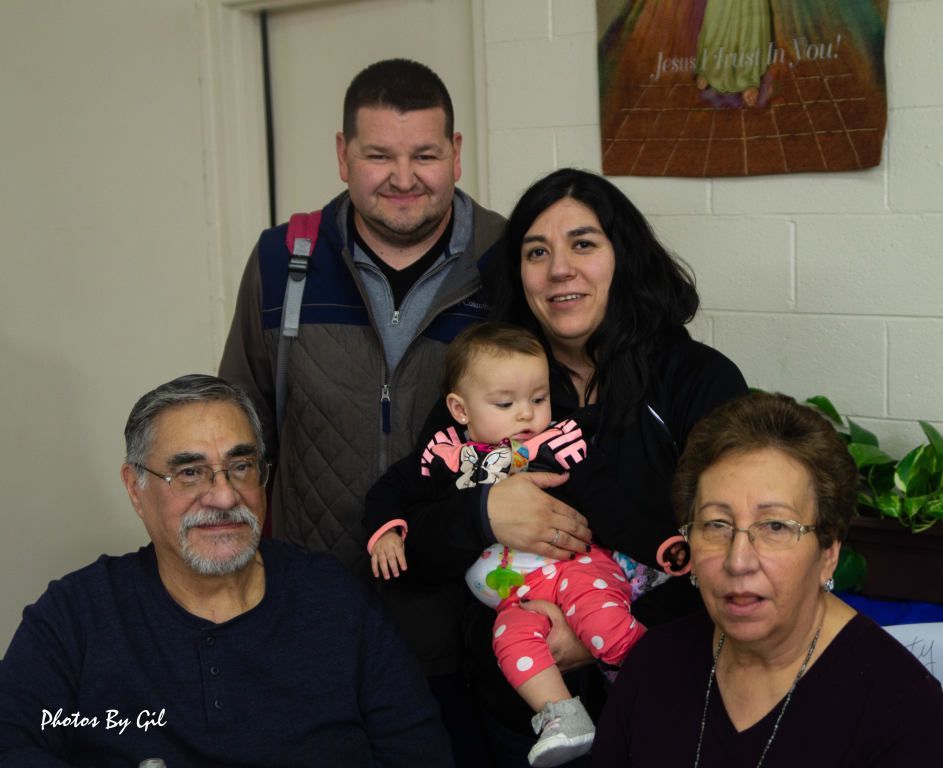 A family of five poses indoors against a white wall.