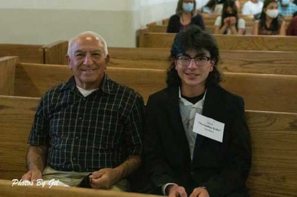 Two people sit in a wooden pew inside a church. 